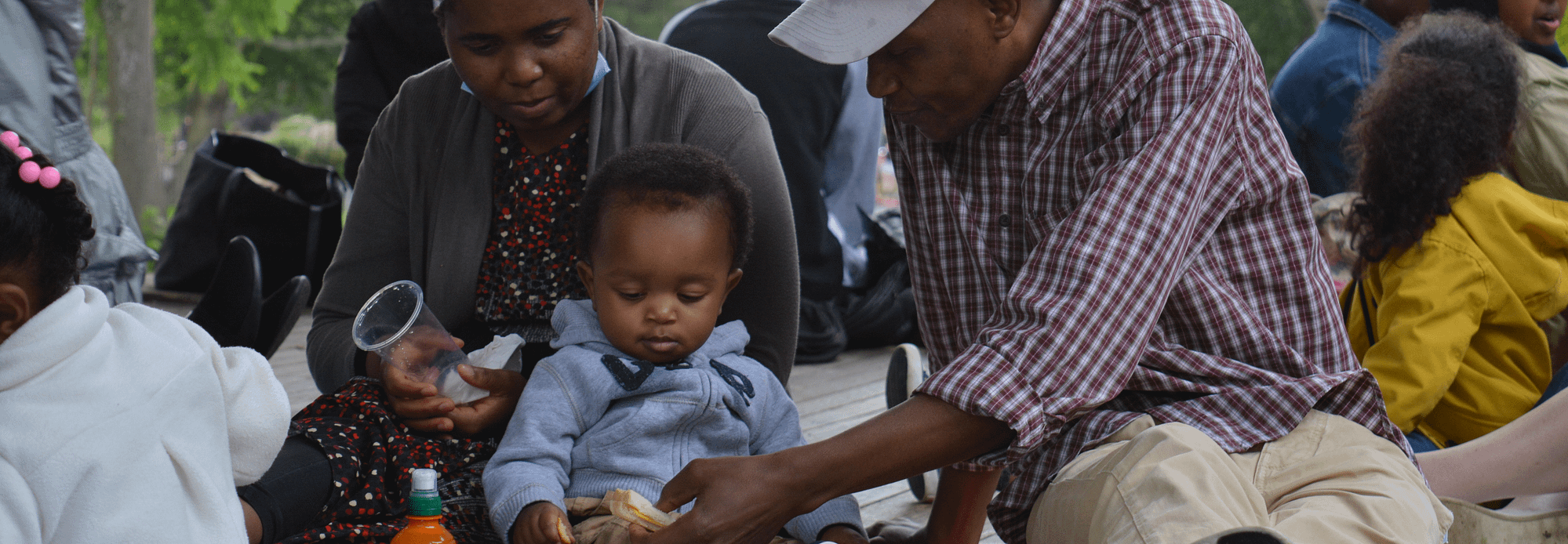 Father feeding young child at a picnic Father feeding young child at a picnic. Mother is watching on.